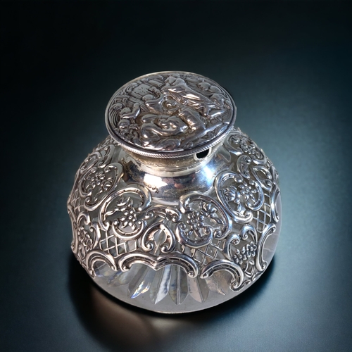 89 - AN EDWARDIAN WILLIAM COMYNS  & SONS REPOUSSÉ SILVER & CRYSTAL INKWELL, WITH WATCH HOLDER TO LID. 
LO... 