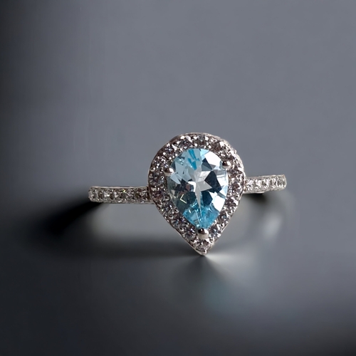 110A - A WHITE GOLD ON STERLING SILVER LADIES RING. SET WITH A CENTRAL PEAR CUT BLUE TOPAZ.