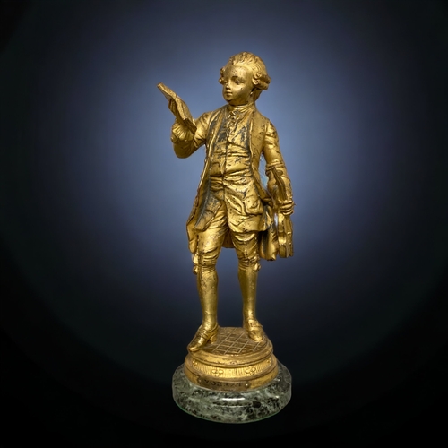 239 - A GILT BRONZE FIGURE OF A YOUNG MOZART. AFTER EMILE BRUCHON. ON MARBLE BASE. 325.CM TALL.