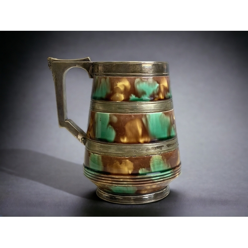 553 - WEDGWOOD TANKARD WITH SILVER PLATE MOUNTED BANDS AND EGYPTIAN DESIGN HANDLE OVER MOTTLED GLAZE.
HEIG... 