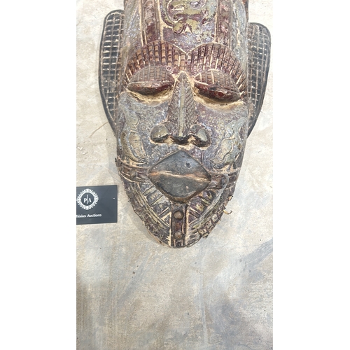 244 - Carved wooden Teak tribal mask adorned with cowrie shells, featuring intricate detailing and a patin... 