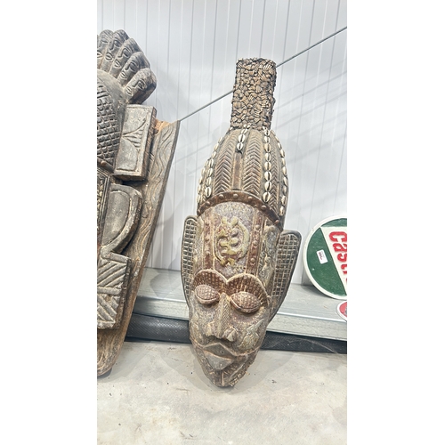 119 - Carved wooden Teak tribal mask adorned with cowrie shells, featuring intricate detailing and a patin... 