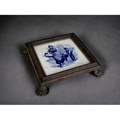 148 - A Painted Delft Tile Trivet Stand.
19th Century. 
Wood framed, with gilt metal Lion paw feet. 
5 x 2... 