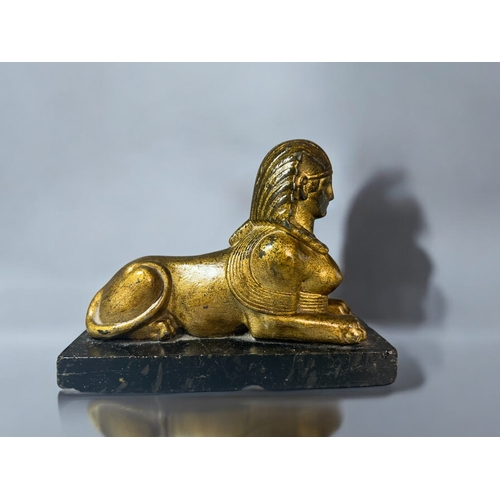 615 - A gilt metal figure of a Sphinx.Mounted on black marble base. 15 x 12cm