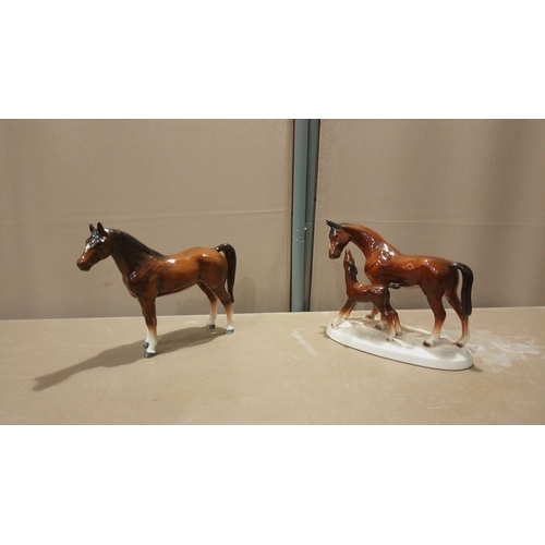 107 - Two porcelain horse figurines: a standing horse and a mare with foal on a plinth. Hand-painted with ... 