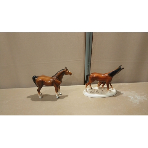 107 - Two porcelain horse figurines: a standing horse and a mare with foal on a plinth. Hand-painted with ... 