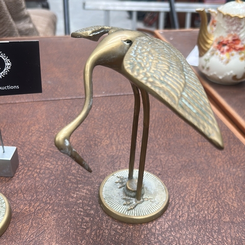 60 - Pair of cast brass crane statuettes, one standing erect, the other bending to feed, each on a textur... 