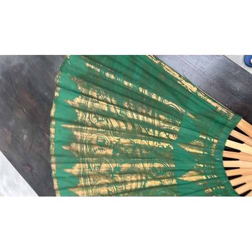 56 - Oversized folding wall fan of bamboo ribs and green fabric leaf, gilt-printed with stylised Thai tem... 