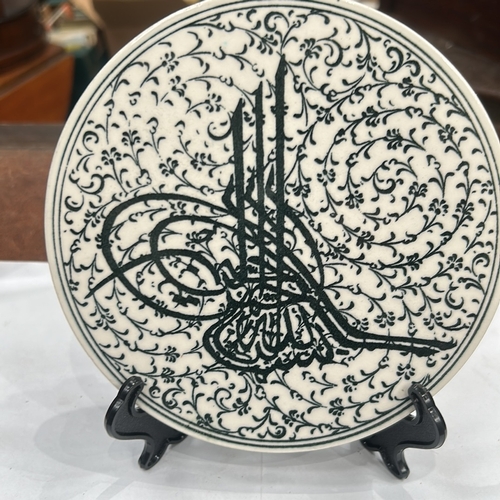 127 - Glazed ceramic round plate decorated in black with an Ottoman tughra surrounded by dense arabesque f... 