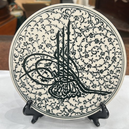 127 - Glazed ceramic round plate decorated in black with an Ottoman tughra surrounded by dense arabesque f... 