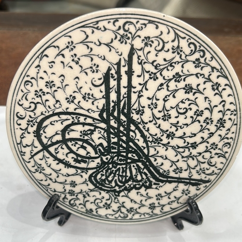127 - Glazed ceramic round plate decorated in black with an Ottoman tughra surrounded by dense arabesque f... 