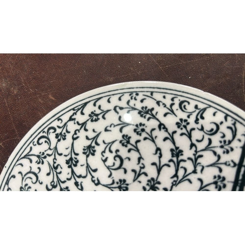 127 - Glazed ceramic round plate decorated in black with an Ottoman tughra surrounded by dense arabesque f... 