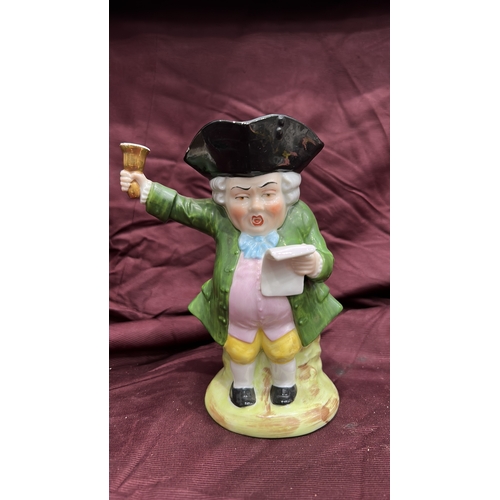 256 - Porcelain character toby jug modelled as a Town Crier with raised bell, tricorn hat forming rim, int... 