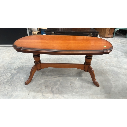 27 - Oval timber coffee table with serpentine-moulded edge top, twin turned column supports united by str... 
