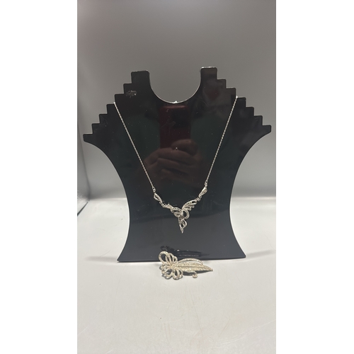 128 - Two silver tone marcasite jewellery items comprising a delicate chain necklace with scrolling ribbon... 