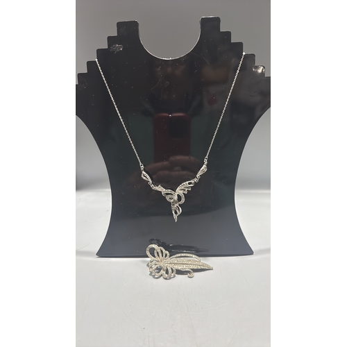 128 - Two silver tone marcasite jewellery items comprising a delicate chain necklace with scrolling ribbon... 