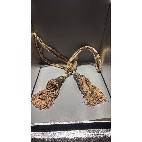 144 - Pair of cream twisted-cord curtain tiebacks, each terminating in an ornate metal mount set with colo... 