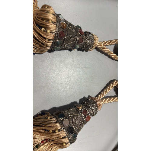 144 - Pair of cream twisted-cord curtain tiebacks, each terminating in an ornate metal mount set with colo... 