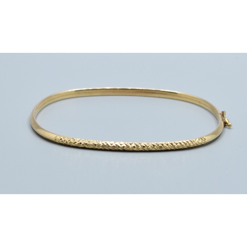137 - 9ct gold oblong bangle with spring closing and safety clip and embossed pattern to one edge  6.3x5.3... 