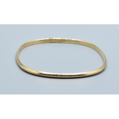 137 - 9ct gold oblong bangle with spring closing and safety clip and embossed pattern to one edge  6.3x5.3... 