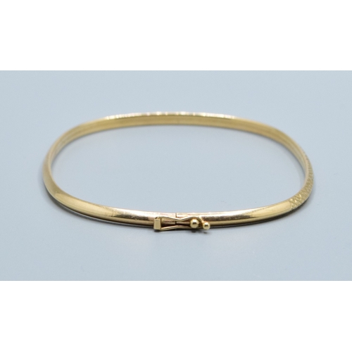 137 - 9ct gold oblong bangle with spring closing and safety clip and embossed pattern to one edge  6.3x5.3... 