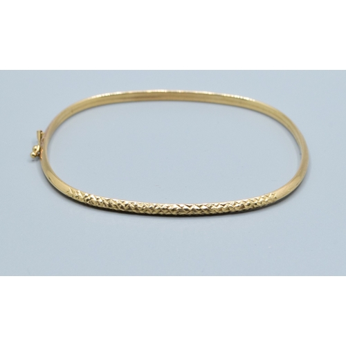 137 - 9ct gold oblong bangle with spring closing and safety clip and embossed pattern to one edge  6.3x5.3... 