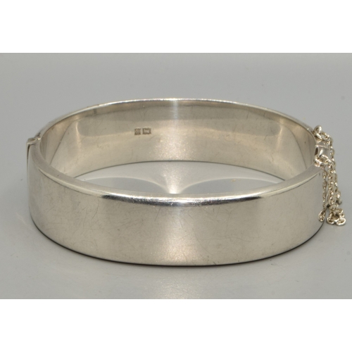 54 - 925 silver ladies bangle with embossed decoration to one side, with safety chain attached 6cm intern... 