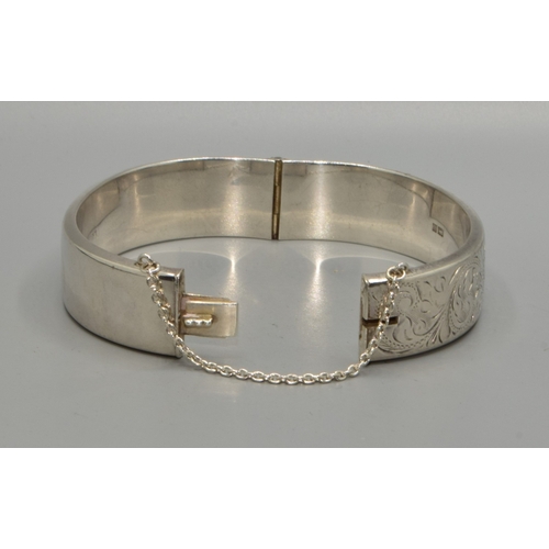54 - 925 silver ladies bangle with embossed decoration to one side, with safety chain attached 6cm intern... 