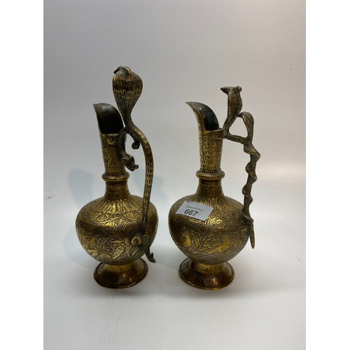 667 - Two intricately carved Arabian brass jugs with Cobra snake handles. 24cm tall.