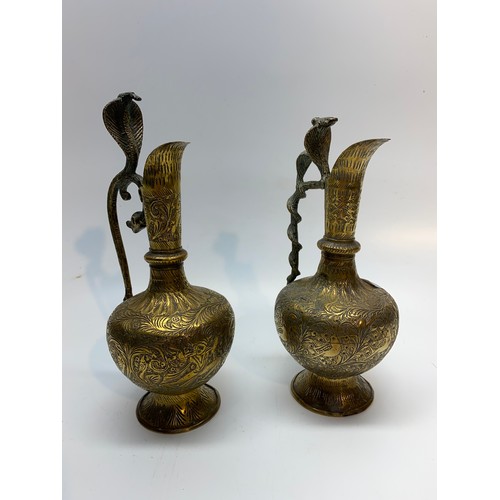 667 - Two intricately carved Arabian brass jugs with Cobra snake handles. 24cm tall.