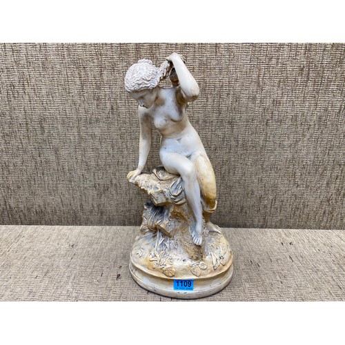 1109 - Porcelain figure of a lady sitting upon a rock; 48cm tall.