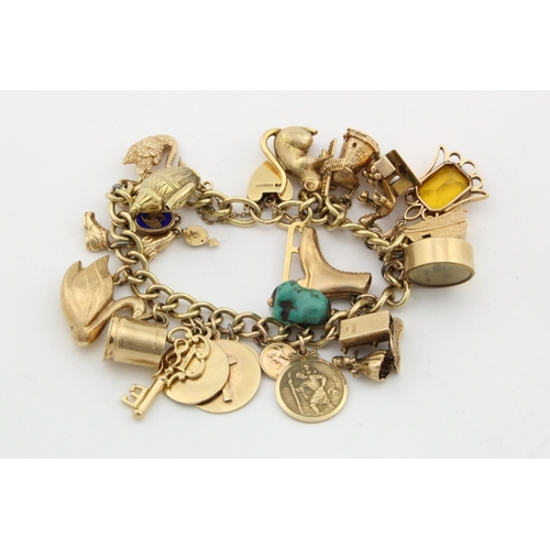 214 - 9ct / Yellow metal charm bracelet with a good selection of charms attached. Total weight 74g