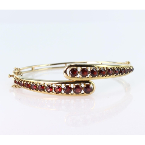 175 - 9ct yellow gold hinged bangle set with twenty two round graduated garnets in a crossover design. Box... 