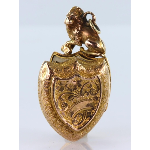 211 - Yellow metal shield shaped locket with machine engraved decoration and topped by a seated lion, meas... 