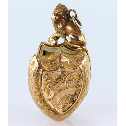 211 - Yellow metal shield shaped locket with machine engraved decoration and topped by a seated lion, meas... 