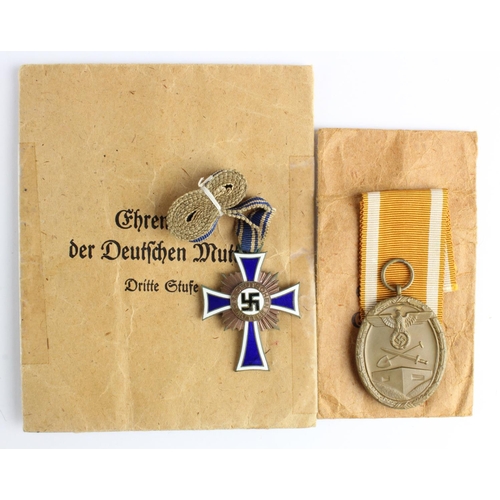 169 - German Nazi Mothers Cross in bronze with paper packet, and West Wall Medal with paper packet. (2)