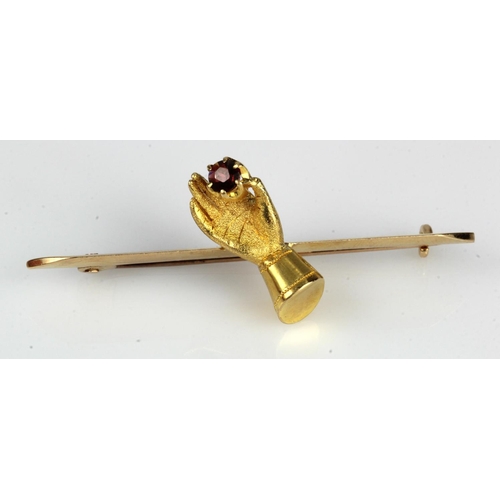 392 - Yellow gold (tests 15ct) bar brooch with (tests 18ct) Victorian hand holding a 3mm garnet, length 50... 