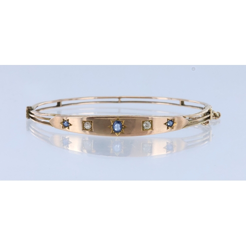 264 - Yellow metal (tests 9ct) hinged bangle with box clasp and safety chain, set with three sapphires and... 
