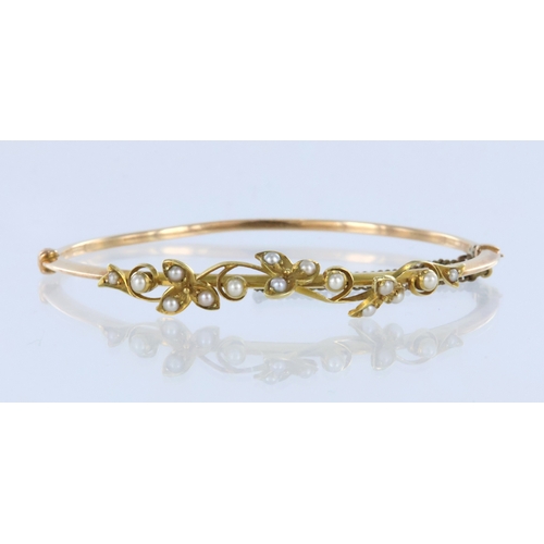 282 - Yellow metal (tests 15ct) hollow hinged bangle in fitted Harrods bangle box, set with fifteen seed p... 