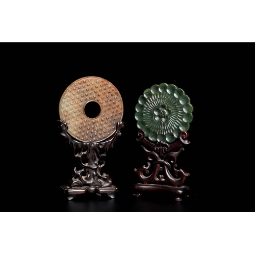 470 - A Chinese celadon and russet jade 'bi' disc and a spinach green flower-shaped pendant on wooden stan... 