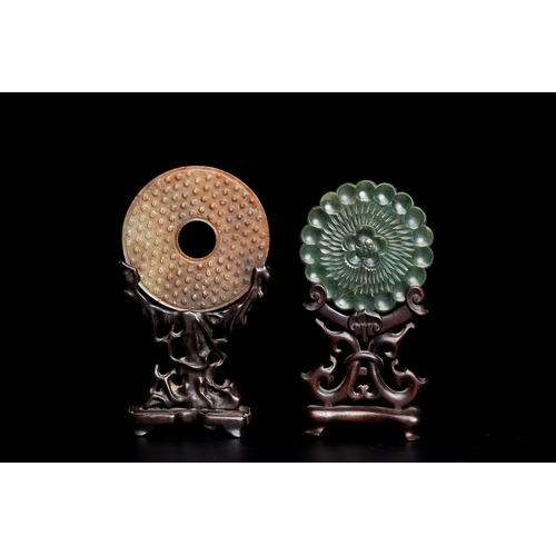 470 - A Chinese celadon and russet jade 'bi' disc and a spinach green flower-shaped pendant on wooden stan... 