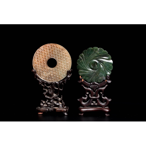 470 - A Chinese celadon and russet jade 'bi' disc and a spinach green flower-shaped pendant on wooden stan... 