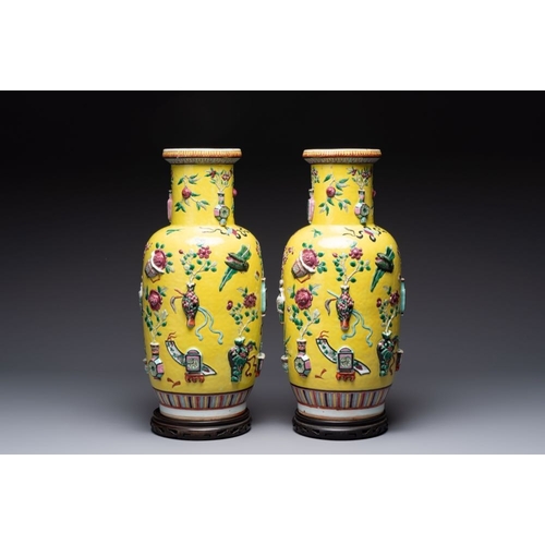 25 - A pair of Chinese famille rose yellow-ground relief-decorated vases with wooden stands, 19th C.H.: 4... 