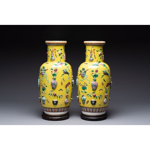 25 - A pair of Chinese famille rose yellow-ground relief-decorated vases with wooden stands, 19th C.H.: 4... 