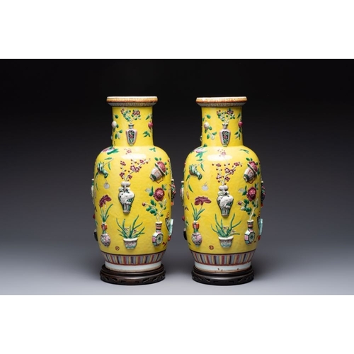 25 - A pair of Chinese famille rose yellow-ground relief-decorated vases with wooden stands, 19th C.H.: 4... 