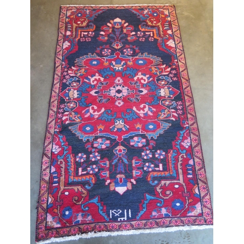 479 - A hand knotted woollen rug with a red field, generally good, some small wear - 204cm x 112cm