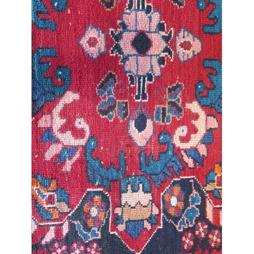 479 - A hand knotted woollen rug with a red field, generally good, some small wear - 204cm x 112cm