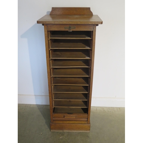 253 - An early 1900s oak filing storage cabinet with a tambour front enclosing nine slides, generally good... 