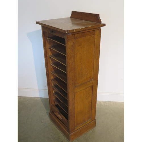 253 - An early 1900s oak filing storage cabinet with a tambour front enclosing nine slides, generally good... 