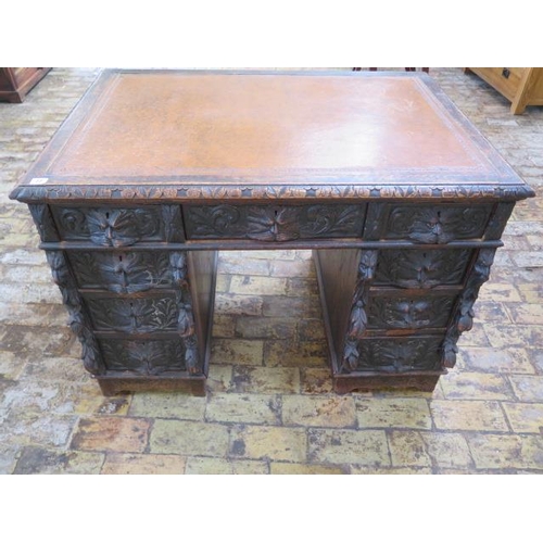 77 - An oak kneehole writing desk with tooled leather top and ornate 'Green Man' carved drawers, 107cm wi... 